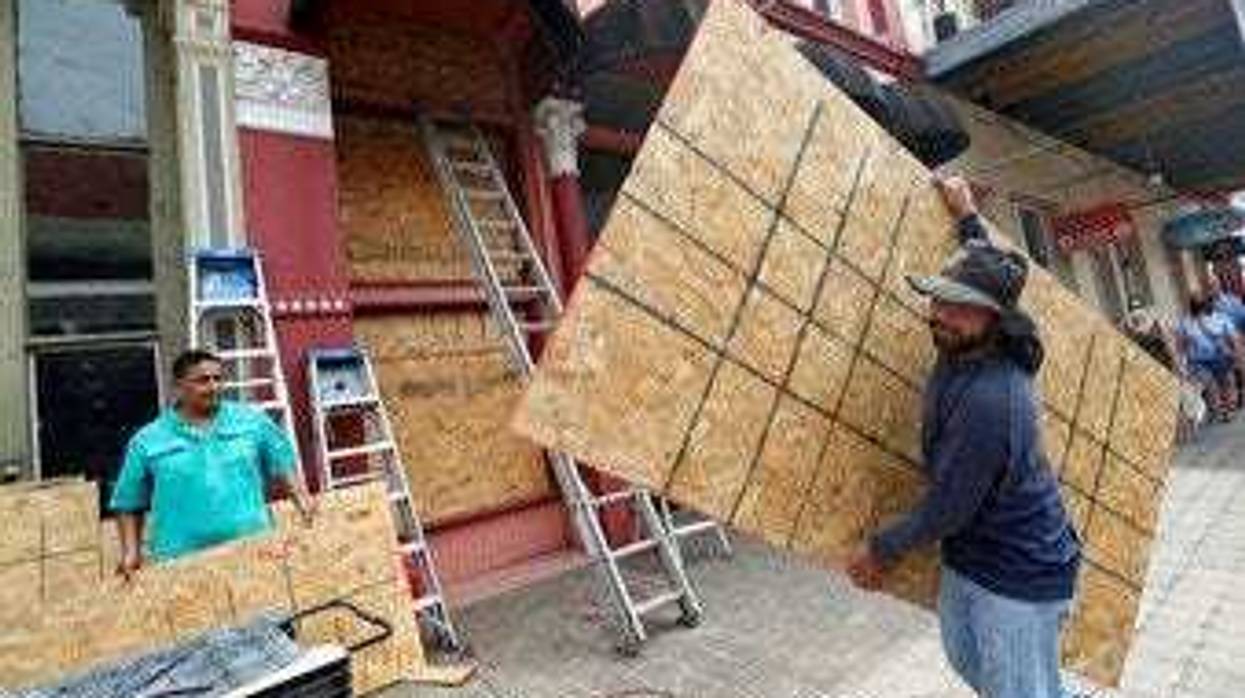 Cesar Reyes carries a sheet of plywood to cut to size as he and Robert Aparicio, left, and Manuel Sepulveda install window coverings at Strand Brass and Christmas on the Strand in Galveston. ( Jennifer Reynolds/The Galveston County Daily News via AP)