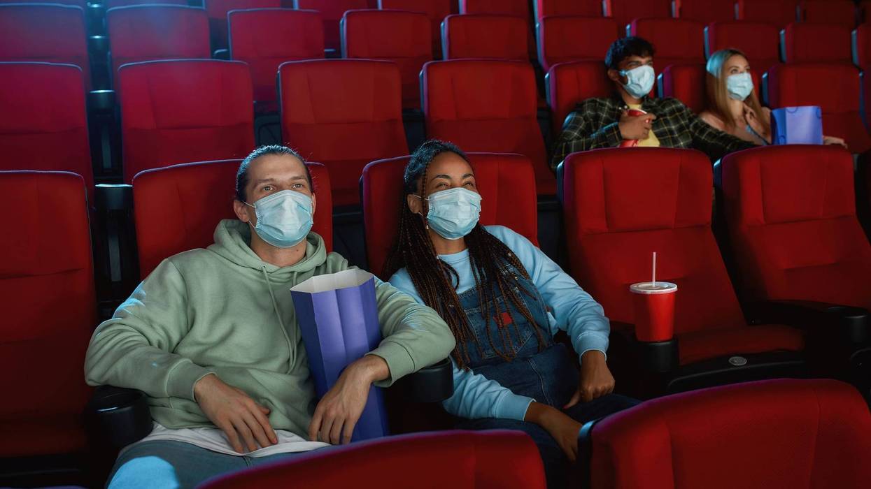 Cheerful young couple wearing face masks for protection from virus disease while watching movie in cinema auditorium. Social distance, entertainment and pandemic concept.
