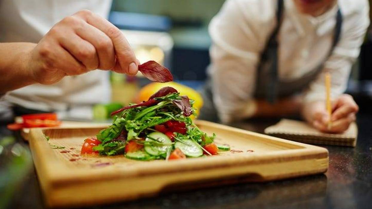 Chef putting leaf of basil on top of vegetable salad