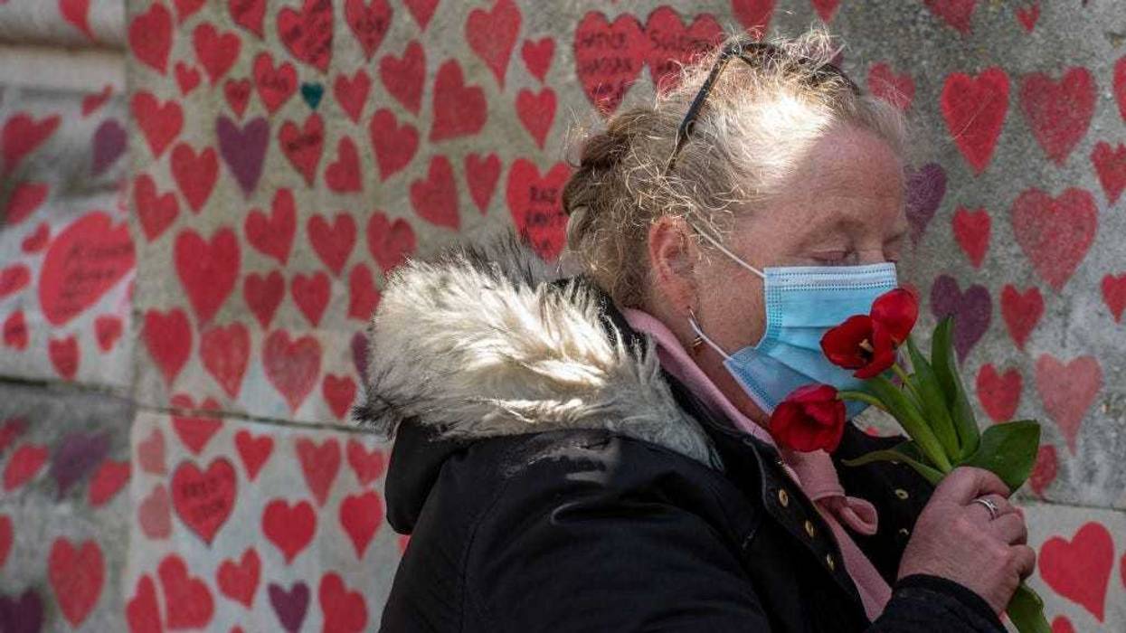 Cheryl Mayne smells tulips that she then leaves next to a heart she drew in memory of her brother Mark Sarnham who died from Covid-19 at the Covid-19 Memorial Wall that is nearing completion opposite Parliament on April 6, 2021, in London, England.