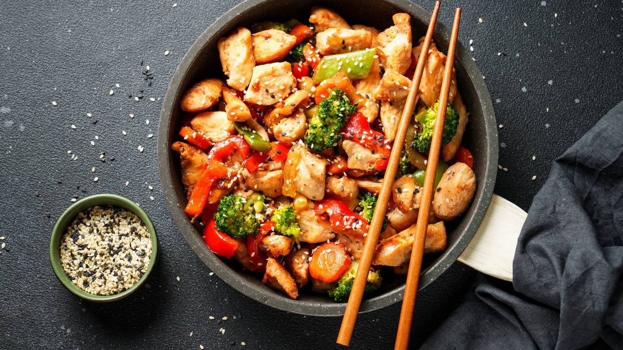 Chicken stir fry with vegetables and sesame in the skillet. Traditional Asian cuisine. Top view at black.
