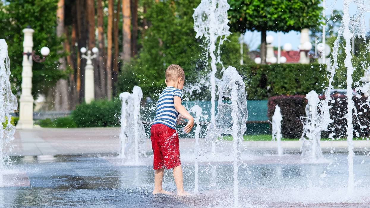 Child playing with water fountain in city square on summer day. Summer lifestyle, joy, freedom and refreshing activity in urban environment.