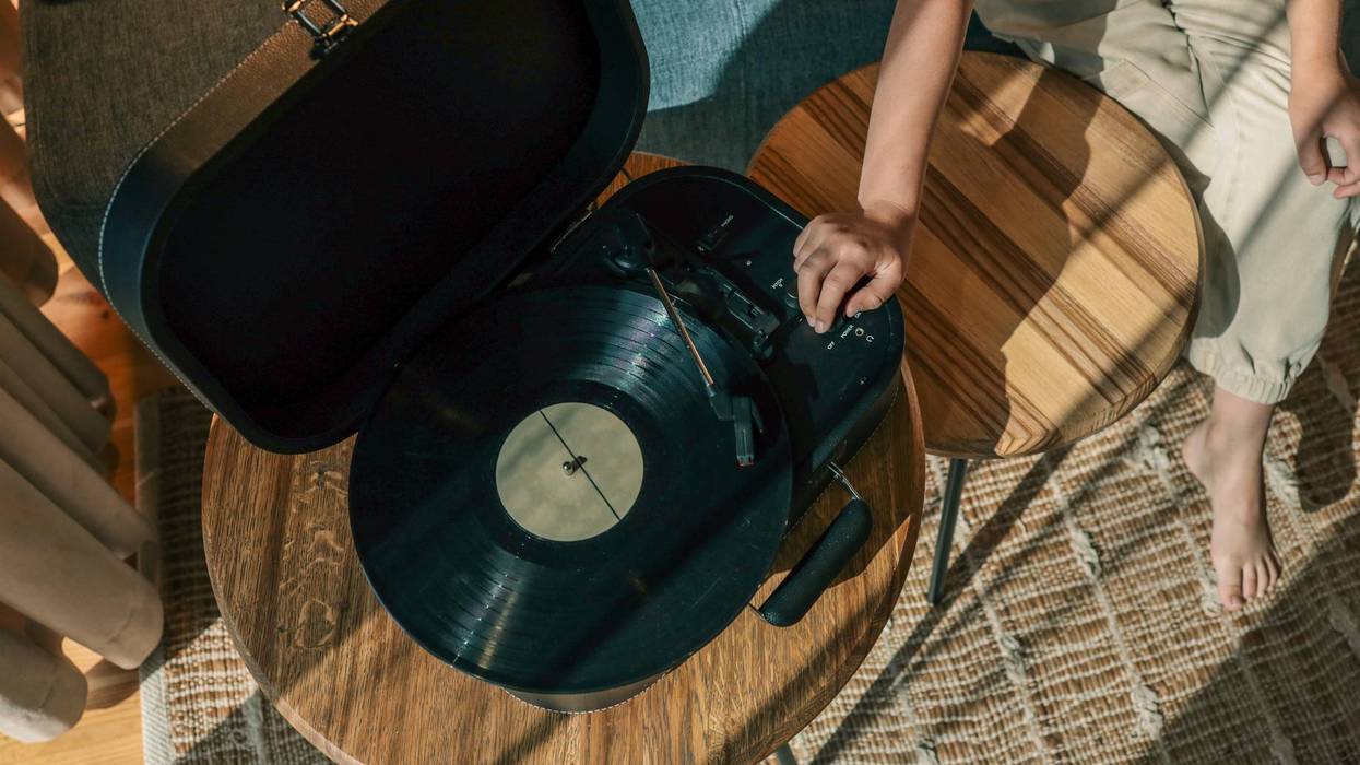 Child turning on turntable with spinning vinyl record, seated barefoot in cozy sunlit living room with wooden furniture