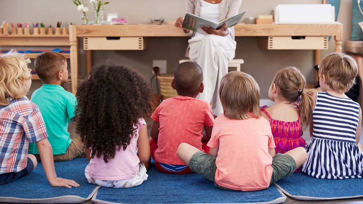 Children sitting on floor in front of a teacher stock photo.