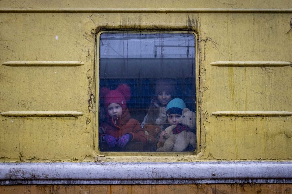 Children Vlada, left, Katrin and Danilo look out from a window of an unheated train carriage of an emergency evacuation train which is travelling from Kharkov to Lviv, as it stopped in the Kyiv railway station in Kyiv, Ukraine, Thursday, March 3, 2022