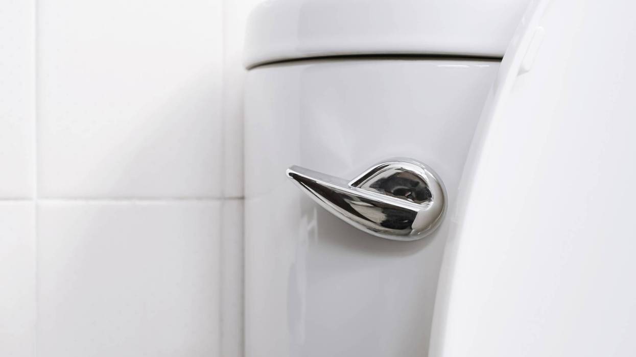 Chrome flush handle on a white toilet tank, with white tiles in the background.