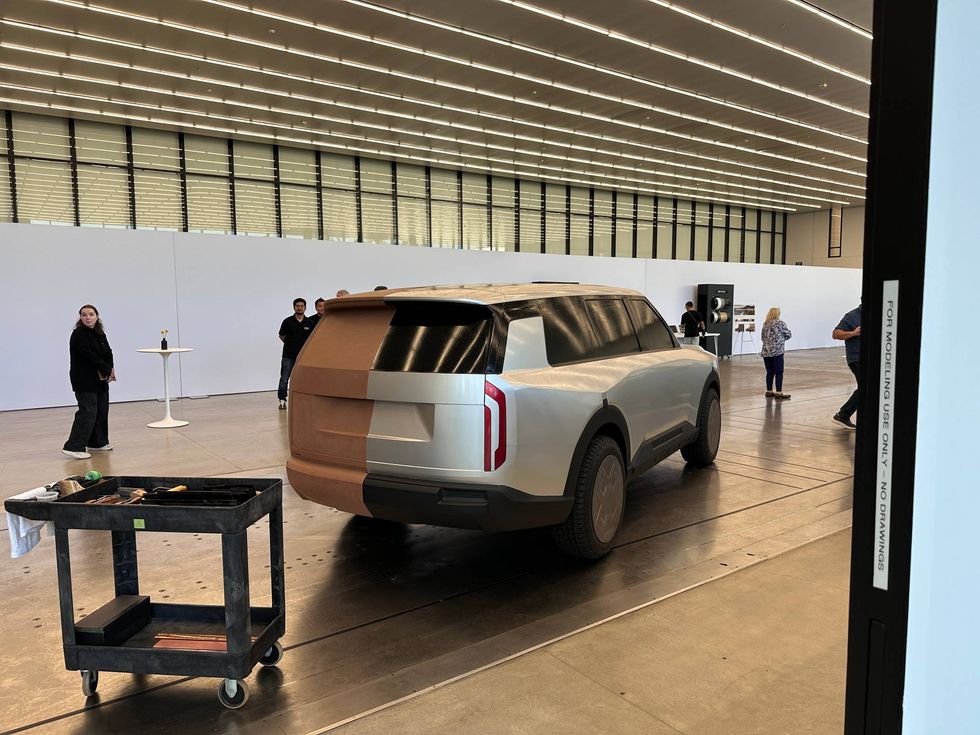 Clay model of a futuristic SUV in a large, well-lit design studio. People observe the model, suggesting a focus on innovation and creativity.