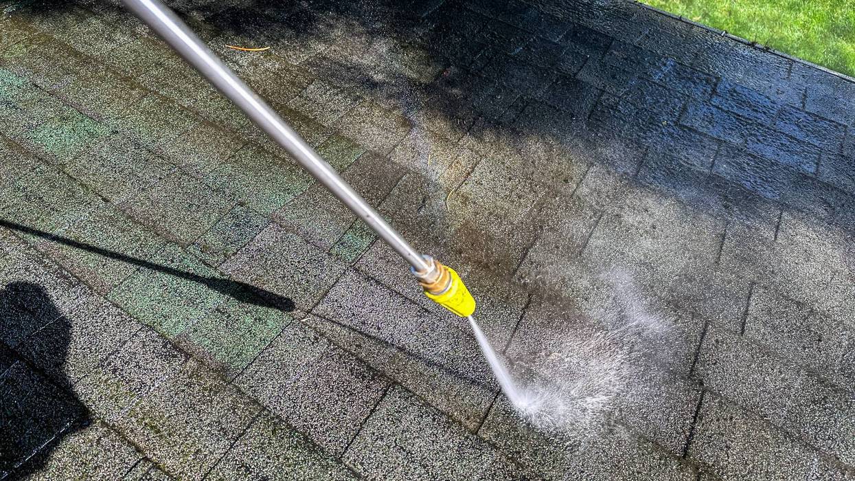 Cleaning a roof with a pressure washer on a sunny day in a backyard