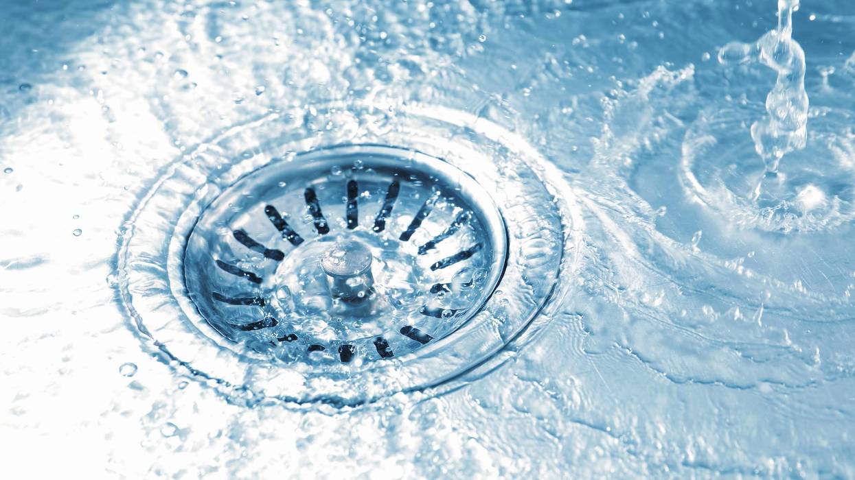 Clear water flowing and splashing into a shiny metal sink drain, creating ripples.