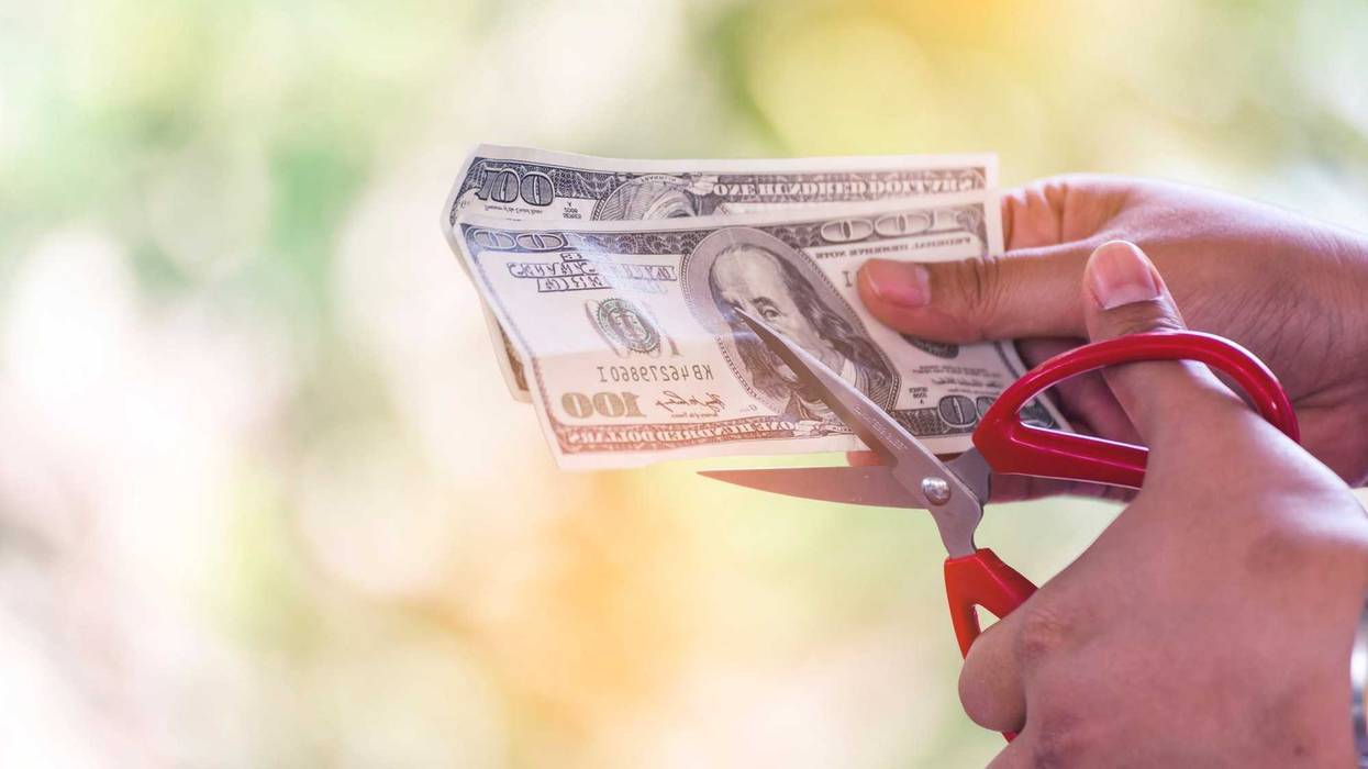 Close up hand cutting money usd banknote. Woman hand cuts money debt with scissors. Close up Hands holding scissors cutting 100 USD money bill. Businessman reduce cost discount