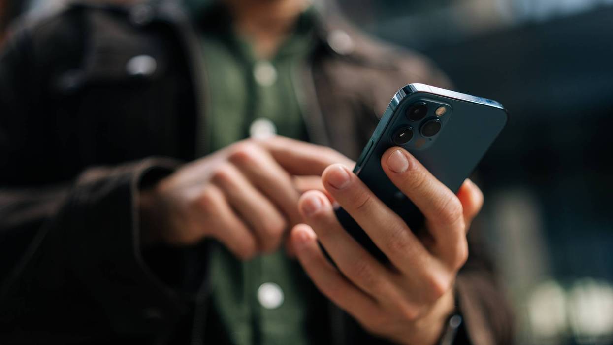 Close-up hands of unrecognizable man holding and using smartphone standing on city street, browsing internet, checking social media, using mobile application.