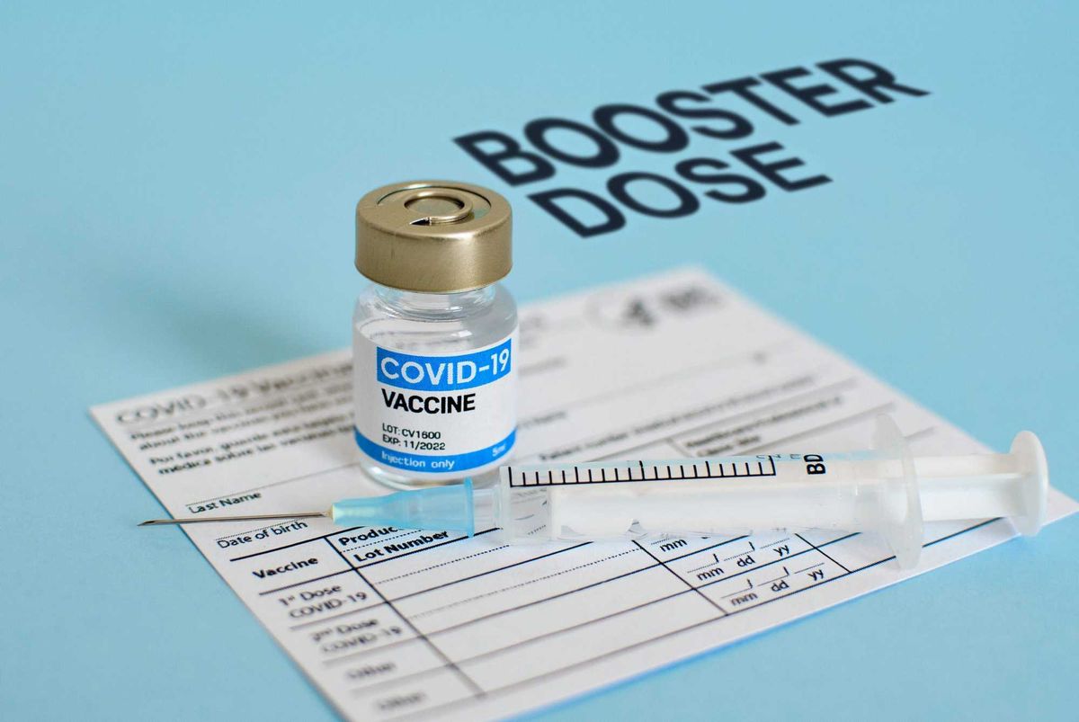 Close-up image of vaccine vial and syringe on CDC covid-19 vaccination record card. Booster dose text on blue background.