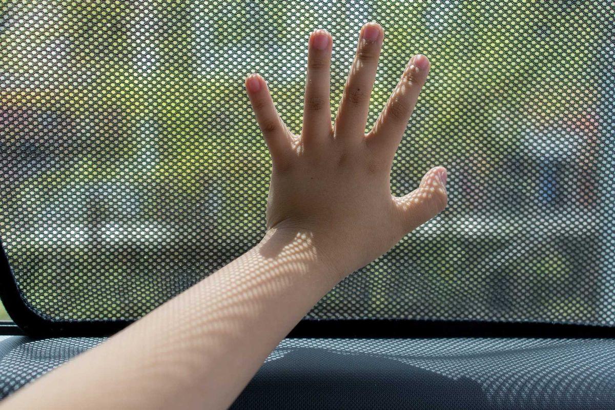 Close up kid hand touching fabric made sunshade in the car side window.