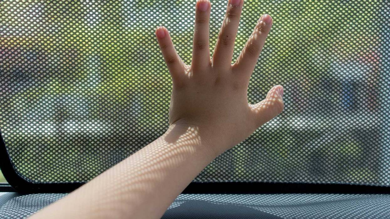 Close up kid hand touching fabric made sunshade in the car side window.