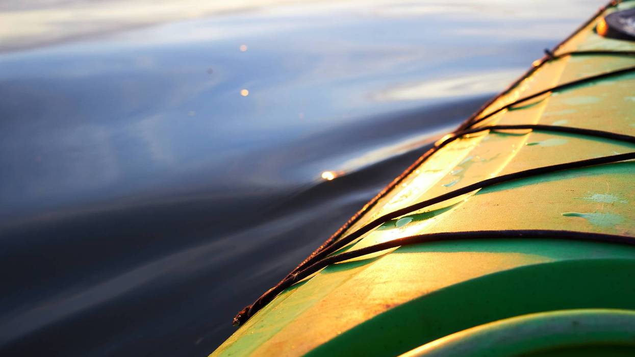 Close-up of a green kayak's side, golden from sunlight, on calm rippled water.
