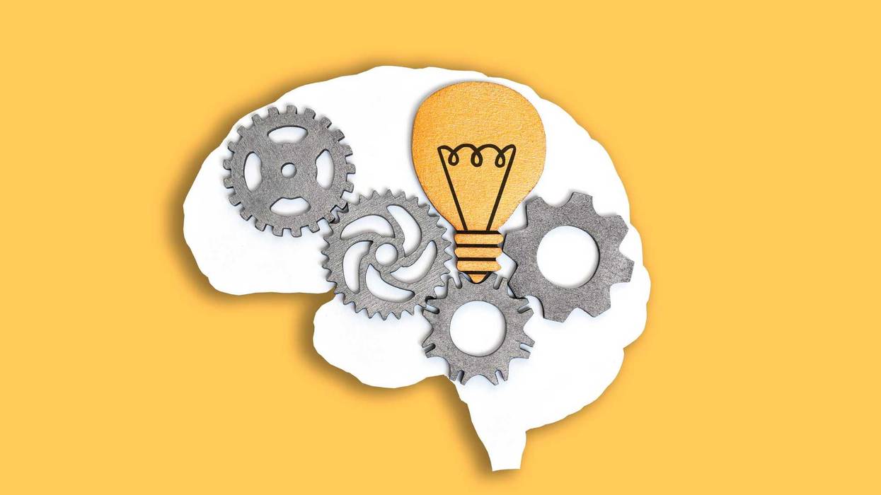 Close-up of a human brain outline with wooden gears and lightbulb isolated on yellow background.