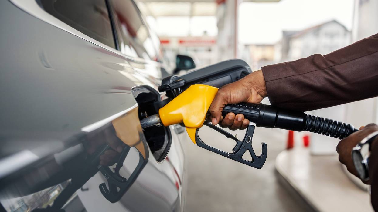 Close up of a man's hand holding nozzle and pouring gasoline at gas station.