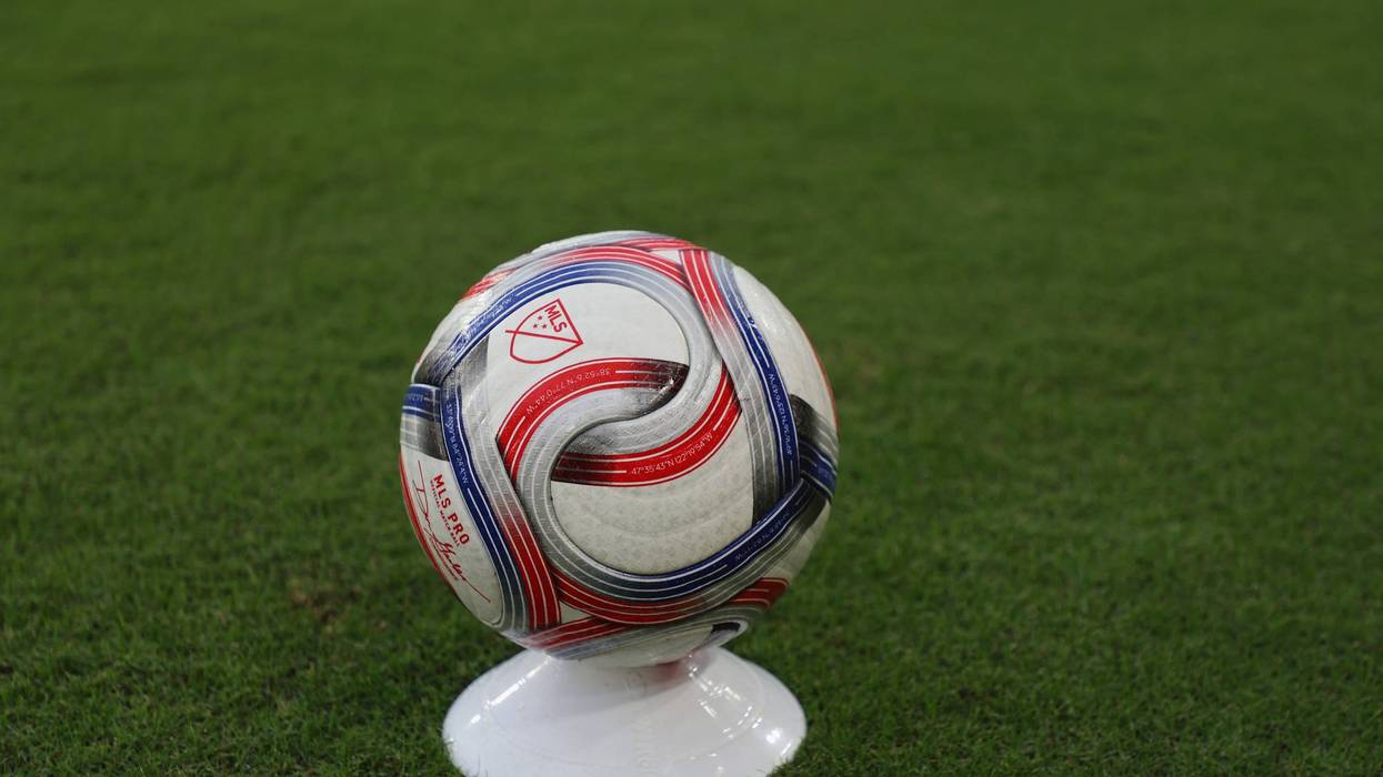 Close-up of a white, red, and blue MLS PRO soccer ball on a stand on green grass.