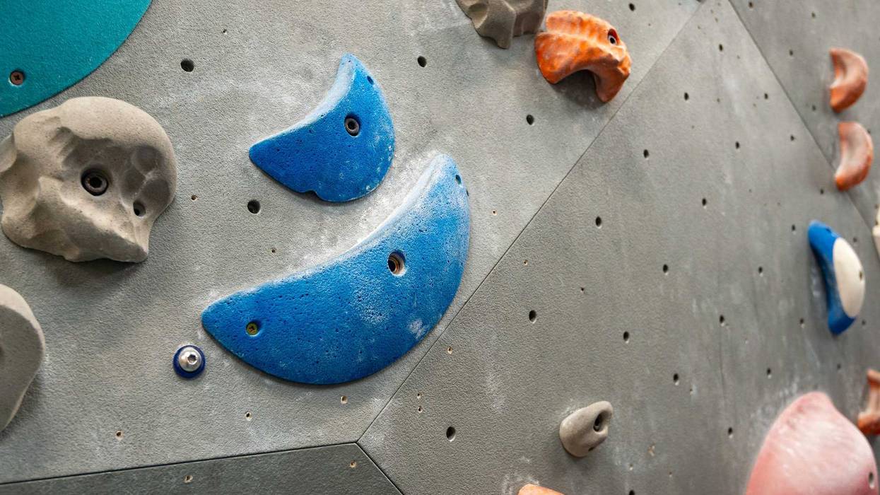 Close up of climbing wall holds and grips of varied shapes and sizes on grey indoor climbing wall at activity centre gym. Blue, red, orange and grey colours.