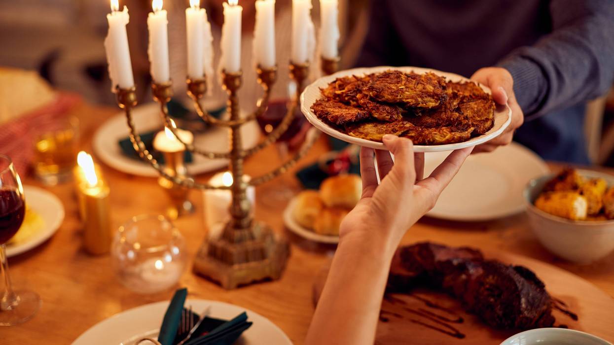 Close-up of couple passing latkes during a meal at dining table while celebrating Hanukkah at home.