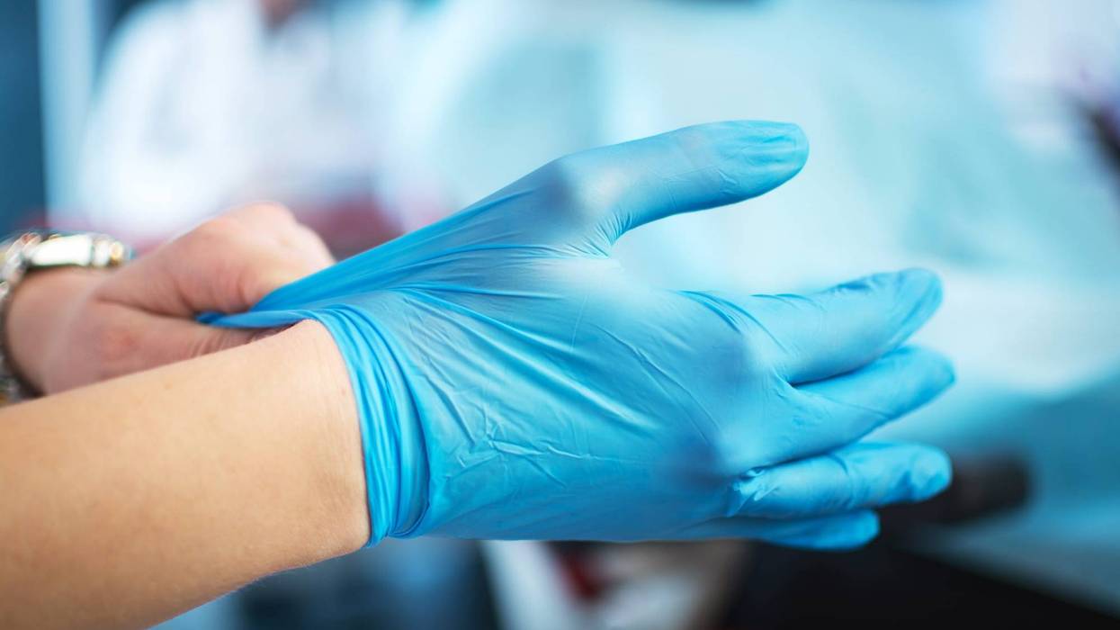 Close up of female doctor's hands putting on blue sterilized surgical gloves in the office.