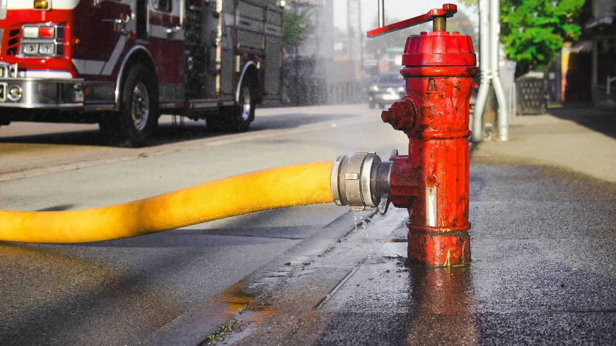 Close up of fire hydrant with hose attached and defocused fire truck.