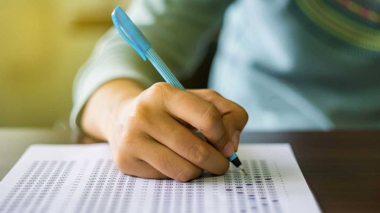 Close up of high school or university student holding a pen writing on answer sheet paper in the examination room. College students answering multiple choice questions test in the testing room in university.
