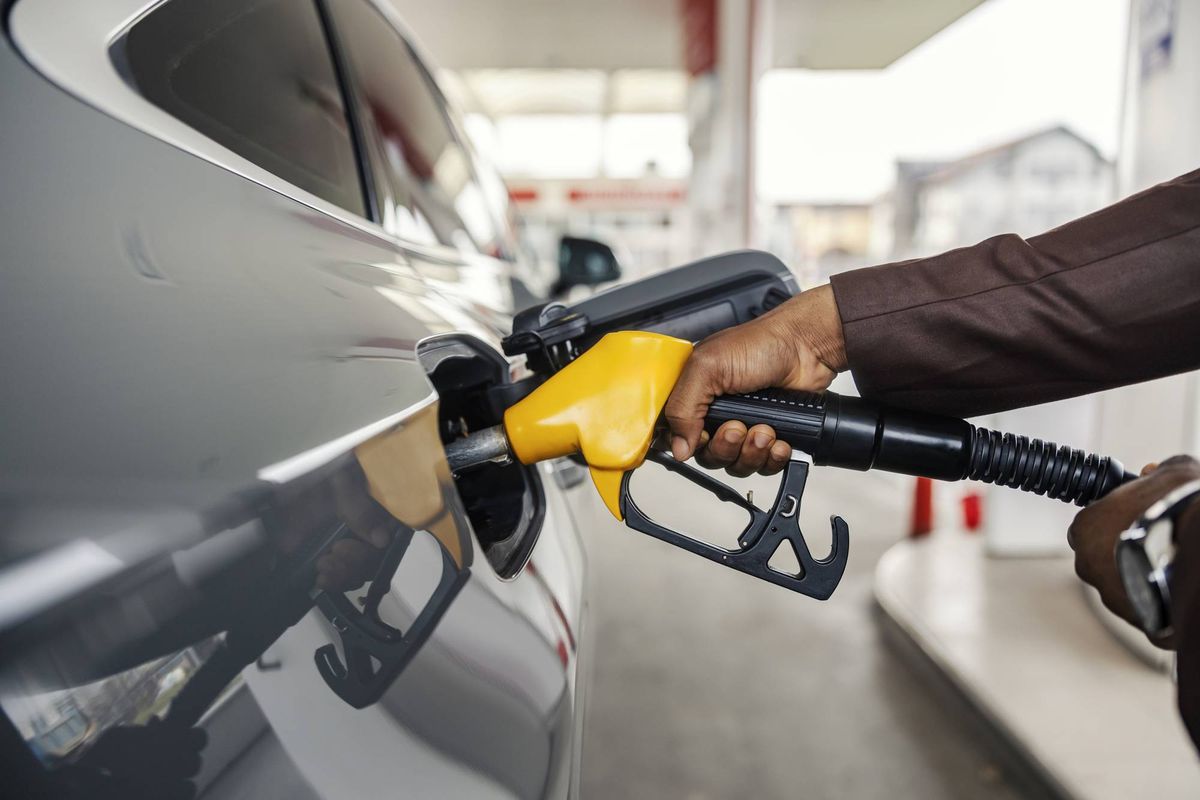 Close up of interracial man's hand holding nozzle and pouring gasoline at gas station.