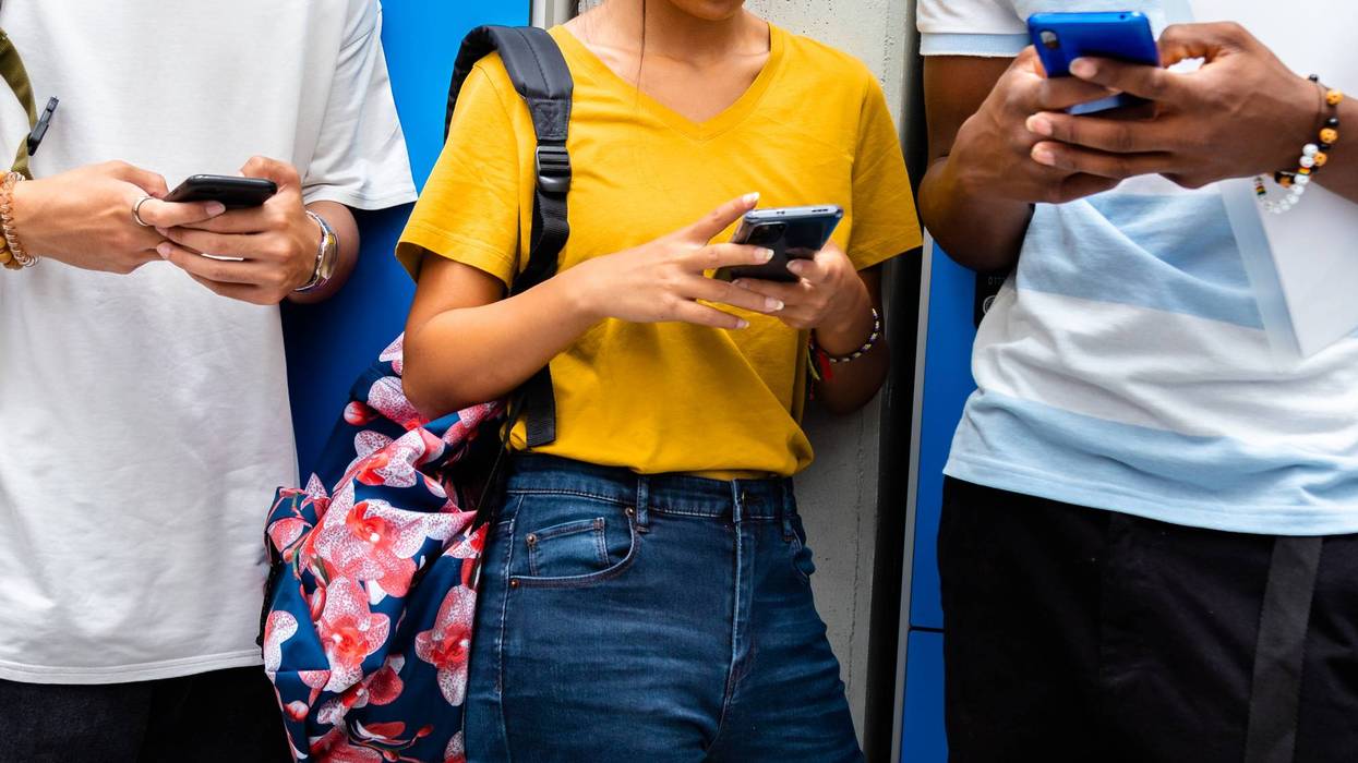 Close-up of teen high school students using mobile phone in school corridor.