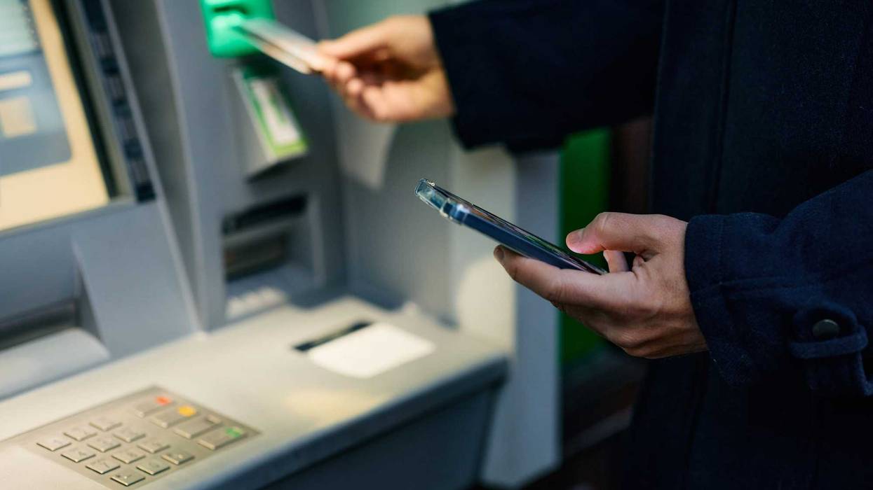 Close up of using cell phone while inserting credit card in ATM machine.