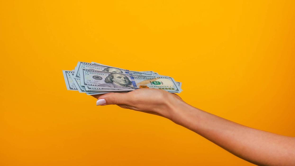 Close up photo of beautiful female hands holding the bunch of dollars of USA isolated on yellow background.