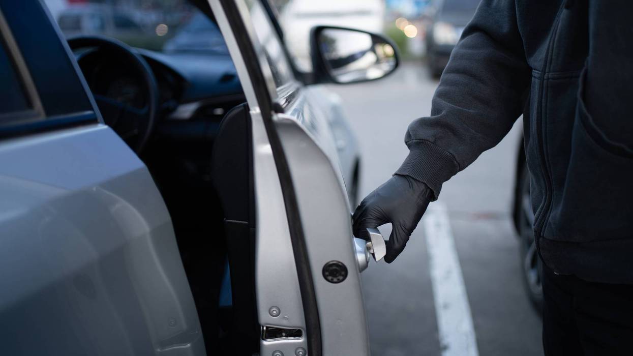 Close-up shot of a thief wearing a black shirt and black gloves. He tries to open the car door and tried to break in.