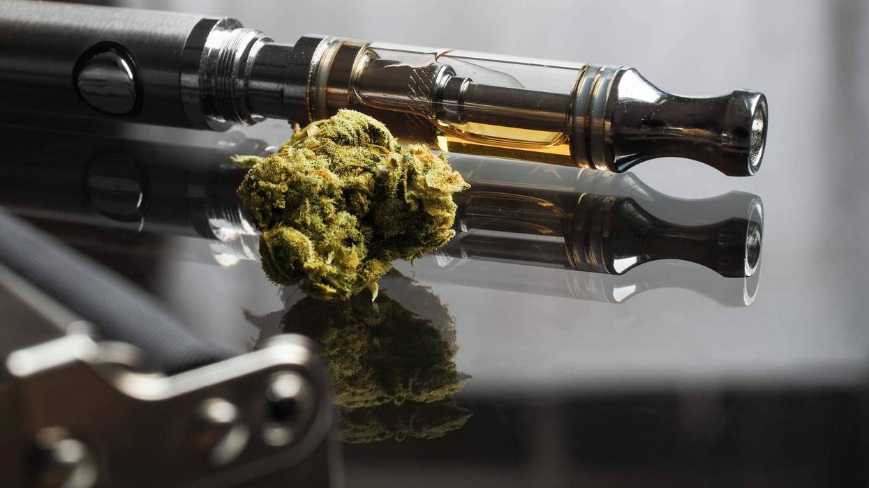Close up shot of real cannabis or weed with cannabis oil in cartridge of vape pen in the background, roller blurred in foreground and text space on the right under the dark theme