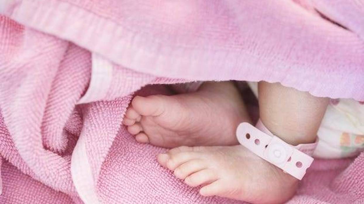 Closeup foot of baby with newborn ankle tag on bed in hospital textured background
