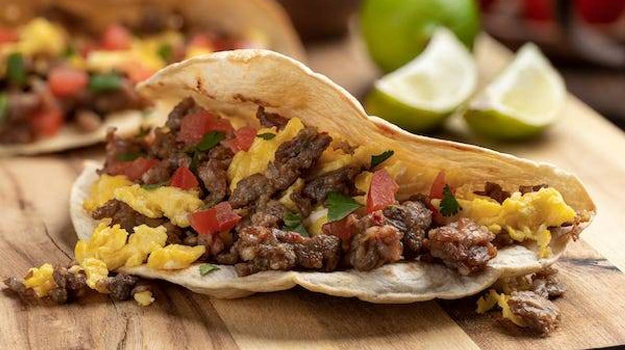 Closeup of a breakfast taco with scrambled egg, sausage and tomato on a wooden cutting board