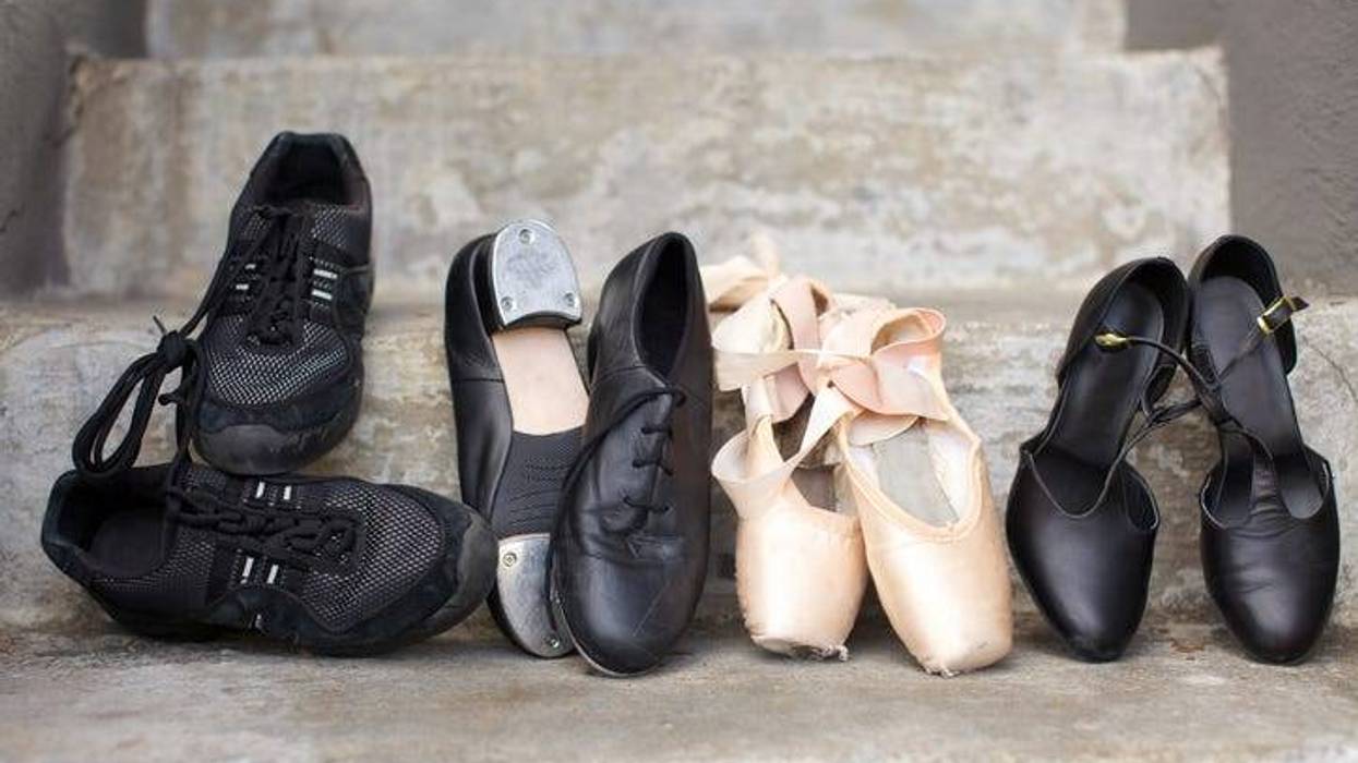Closeup of a pair of jazz shoes, tap shoes, ballet pointe shoes, and character shoes representing a variety of dance classes in one image. Shoes are resting on concrete steps.