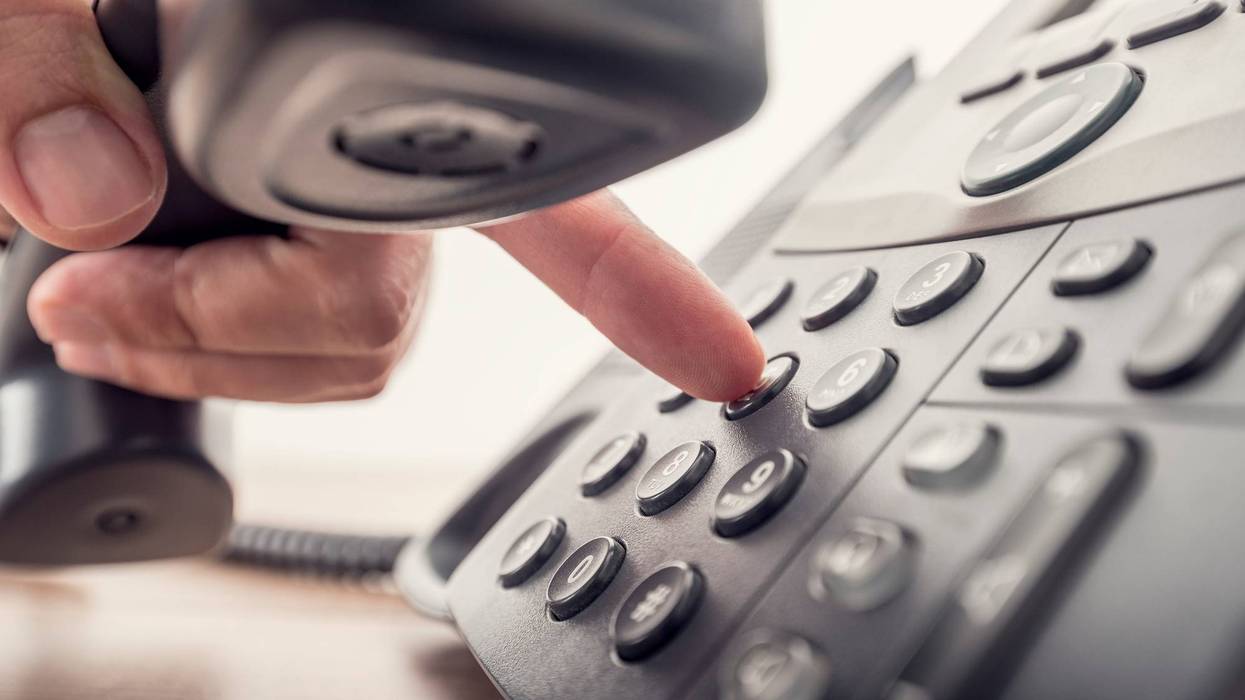 Closeup of hand holding telephone receiver while dialing a number on a black landline phone.