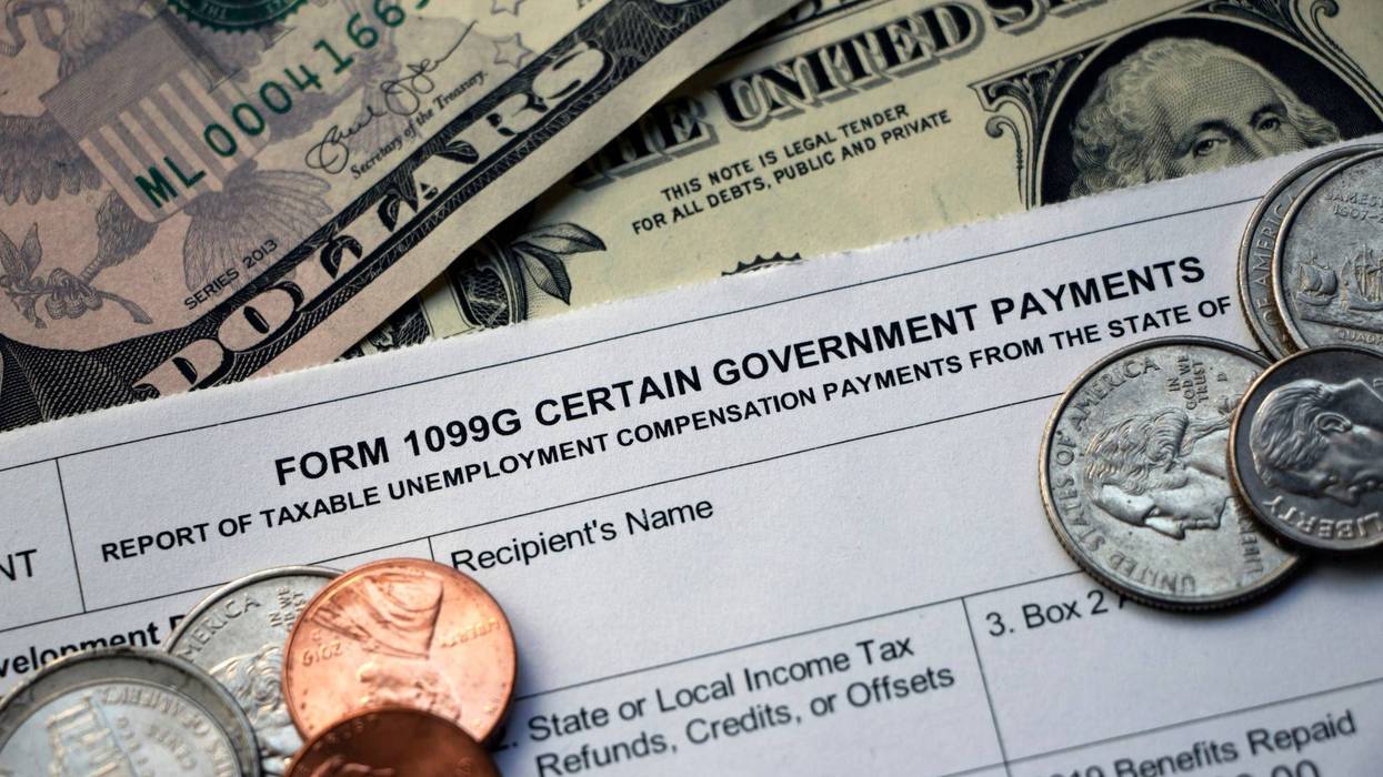 Closeup of the top of a tax Form 1099G Certain Government Payments - Taxable Unemployment Compensation Payments on top of cash with some coins scattered on top.