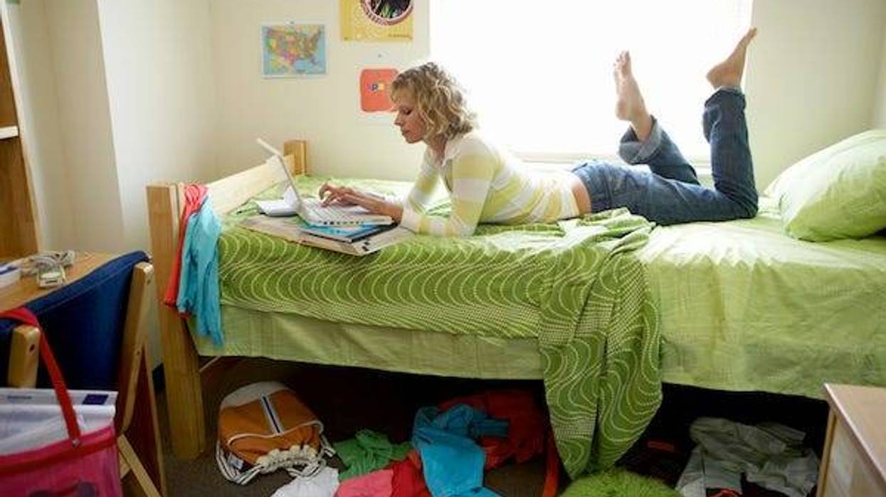 College student lying on bed in messy dorm room