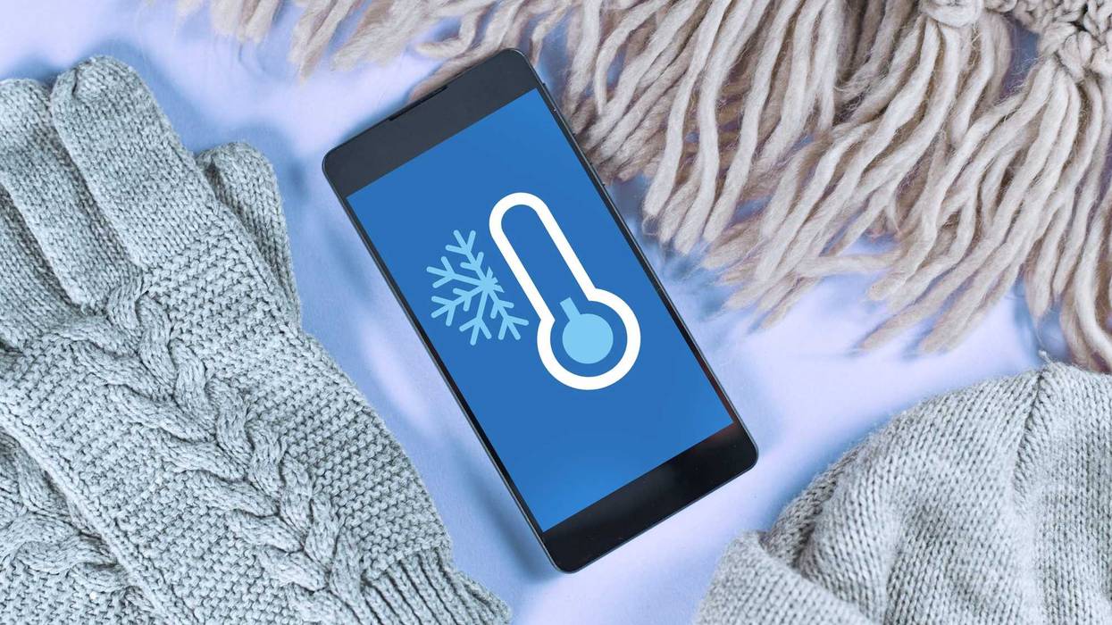 Concept for cold temperatures with snow and minus degrees with mobile phone showing weather forecast surrounded by warm clothes