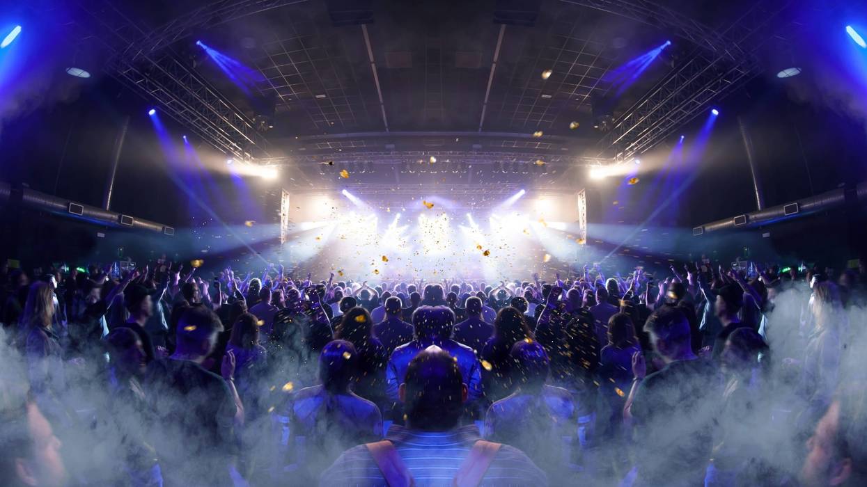 Concert crowd inside a venue, lens flare and smoke are visible.