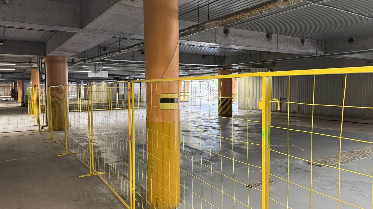 Concrete underground parking garage with orange pillars sectioned off by yellow fences.
