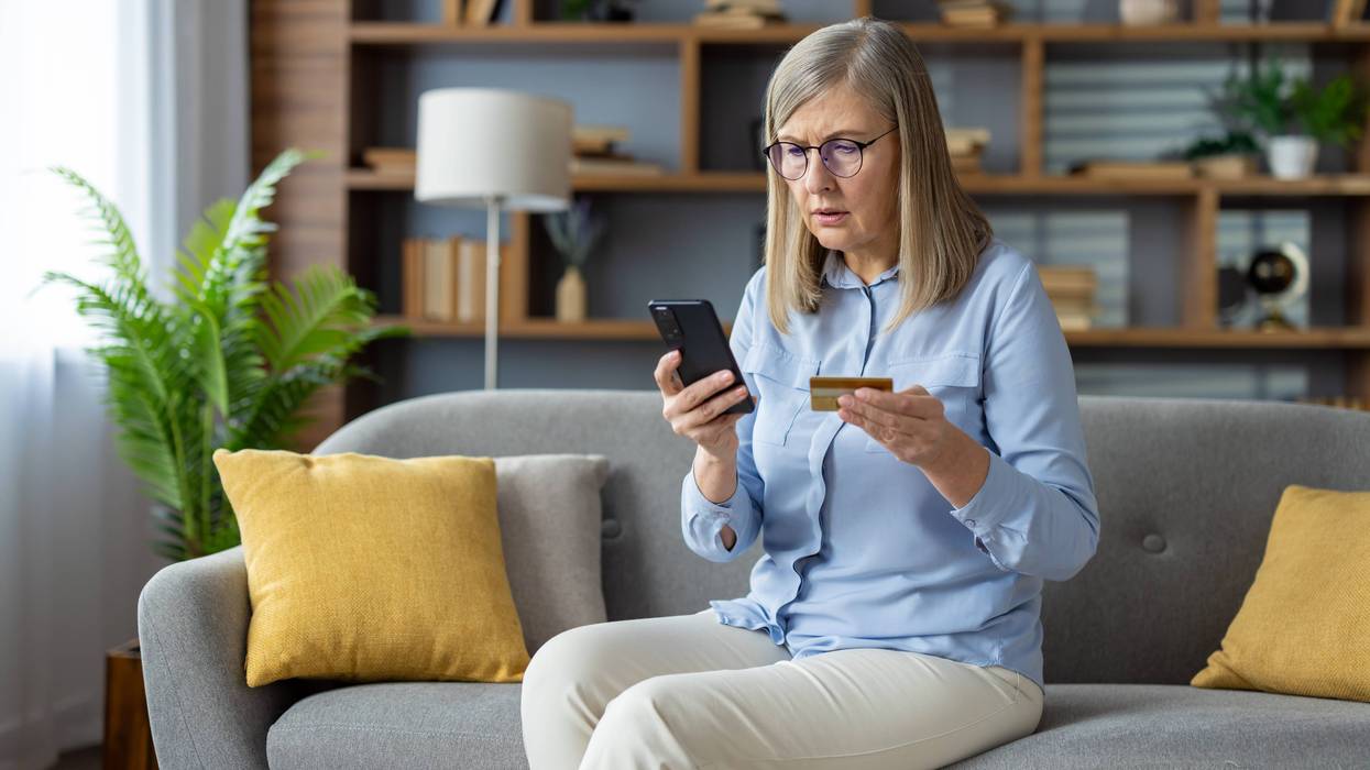 Confused older woman holds credit card in one hand and phone in other