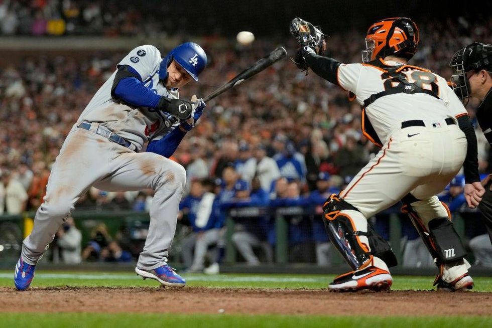 Corey Seager #5 of the Los Angeles Dodgers dodges a pitch in front of Buster Posey #28 of the San Francisco Giants in game 5 of the National League Division Series at Oracle Park.