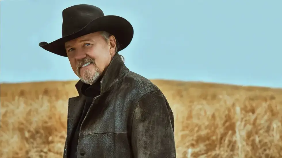 Country singer Trace Adkins in a black cowboy hat and leather jacket, smiling in a golden field.