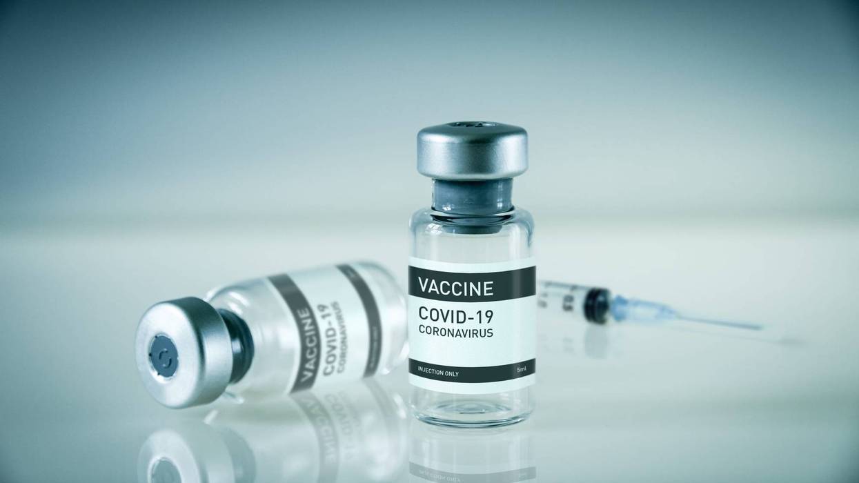 Covid-19 vaccine bottle and syringe on a blue background - stock photo