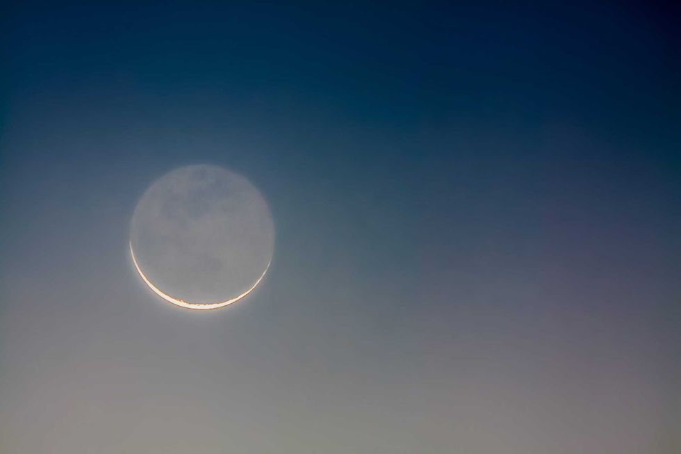 Crescent moon showing earthshine at sunrise
