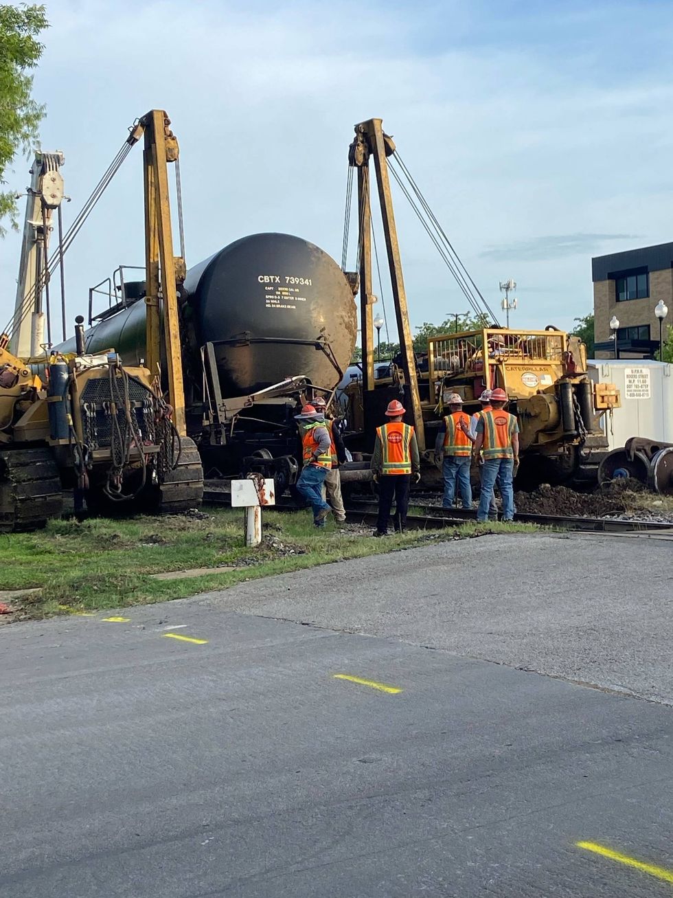 Crews use a crane to right a derailed tanker car