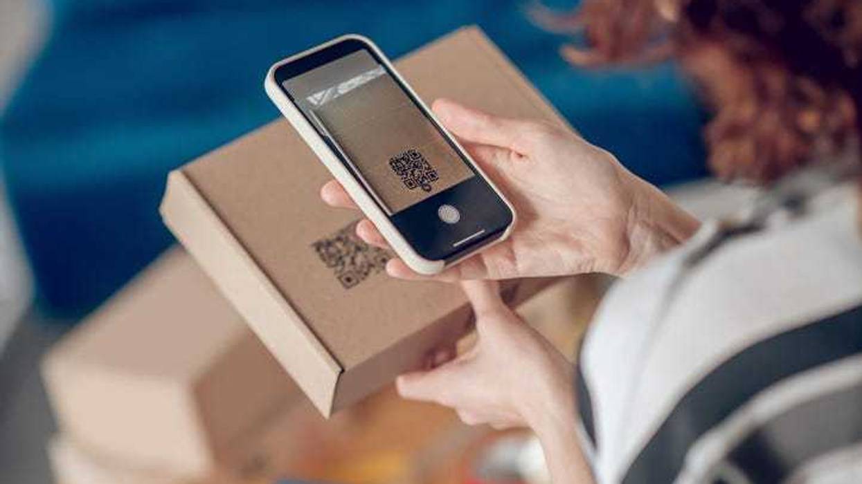 Cropped photo of a female worker aiming her camera at the QR code on the cardboard box