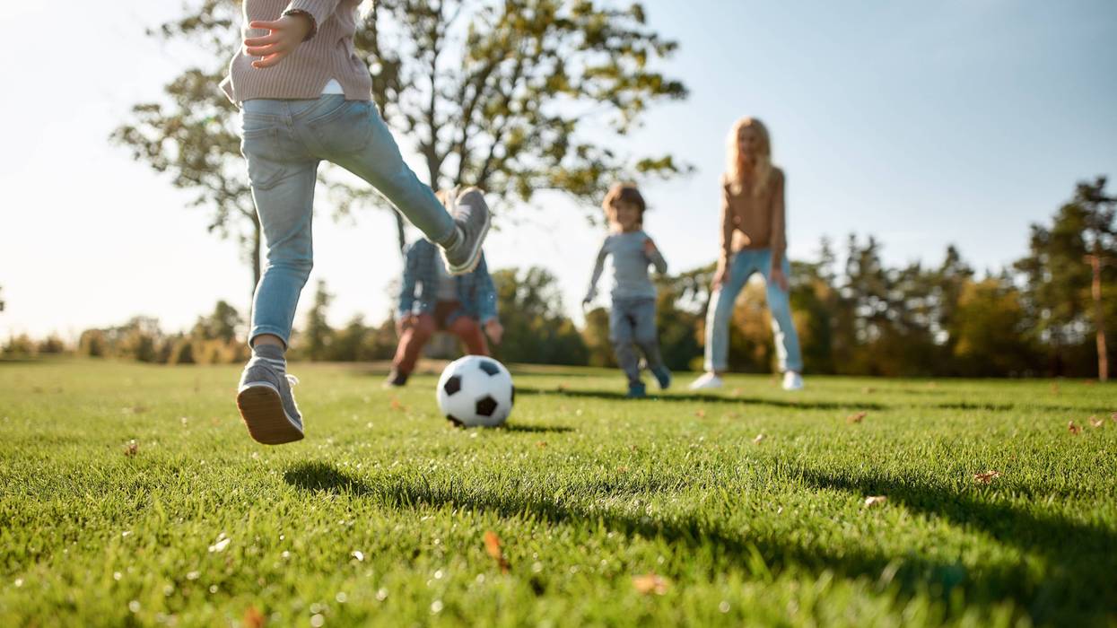 Cropped portrait of cheerful little girl playing football with her family in the park on a sunny day.